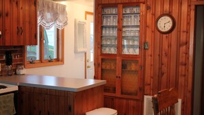 Una cucina con mobili in legno, una finestra con tenda, un orologio a parete e un cestino.