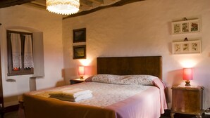 A cozy bedroom with a large bed, two bedside tables with lamps, a wooden headboard, and floral wall decorations. - House-Tower in 15th Century Borgo Fontanini - with mountain views (Zocca)