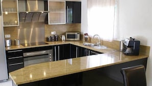 A modern kitchen with a central island, stainless steel appliances, and a window with sheer curtains.