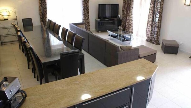 A modern living room with a dining area, a sofa, a TV, and a kitchen area.