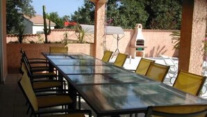 A covered outdoor dining area with a long table and yellow chairs.