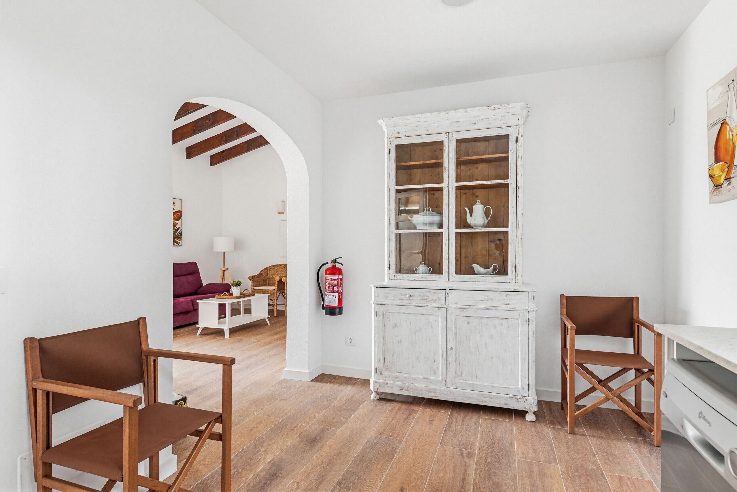 A room with a white cabinet, two wooden chairs, a purple sofa, and a wooden floor.