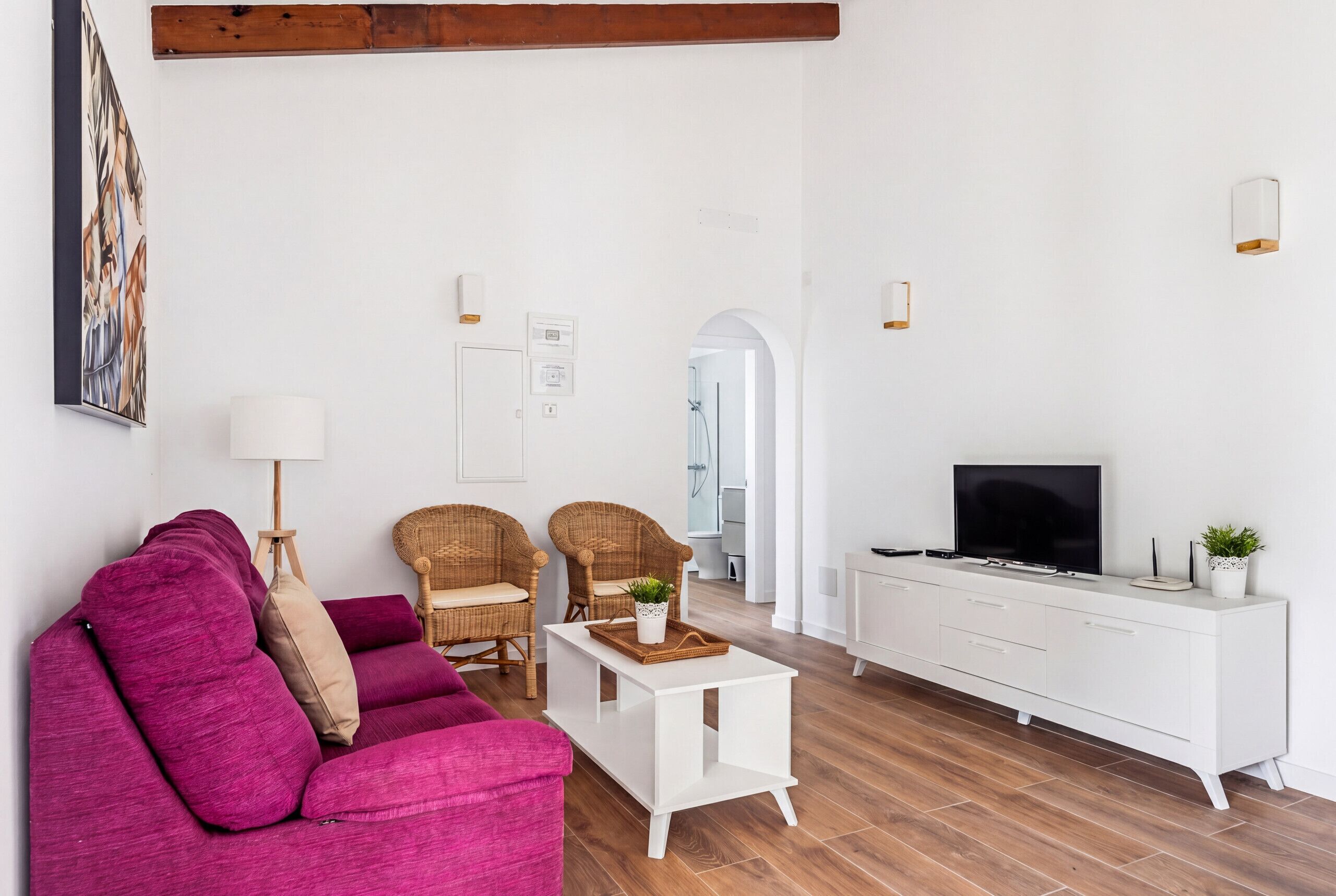 A living room with a sofa, two wicker chairs, a coffee table, a TV, and a white cabinet.
