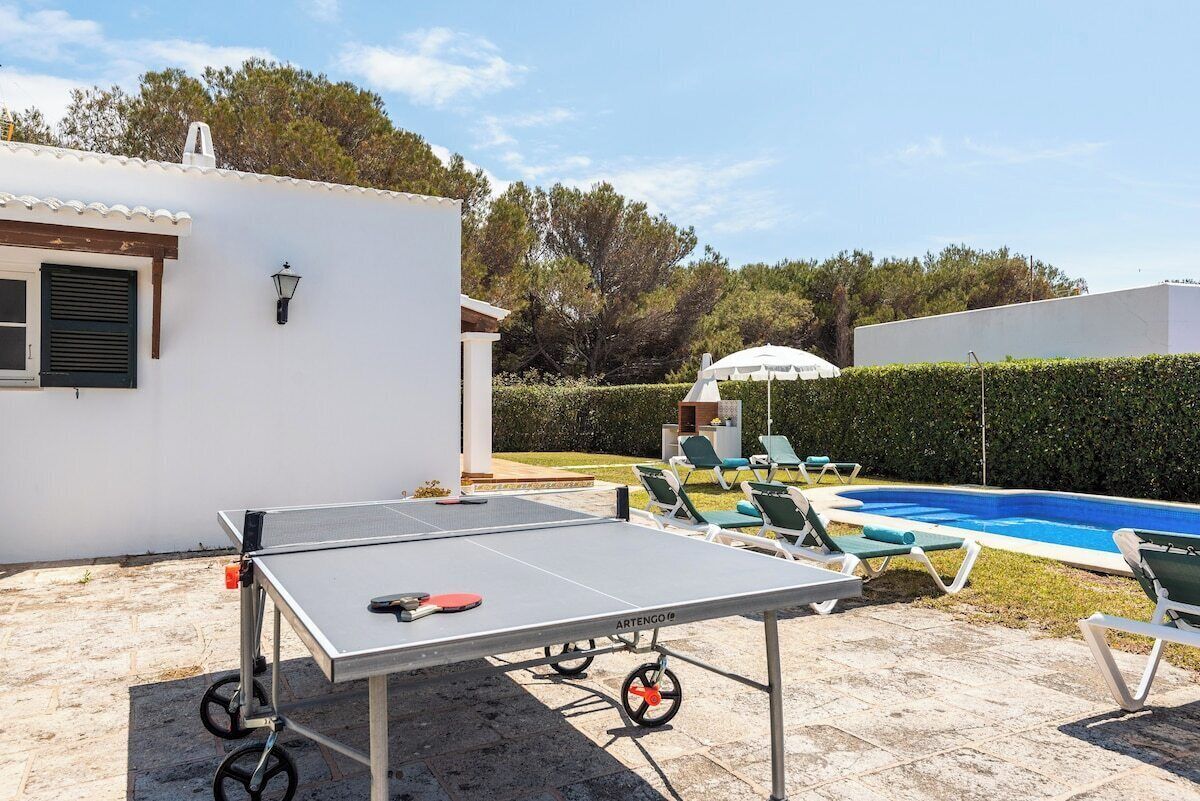A ping pong table in a backyard with a pool and lounge chairs.
