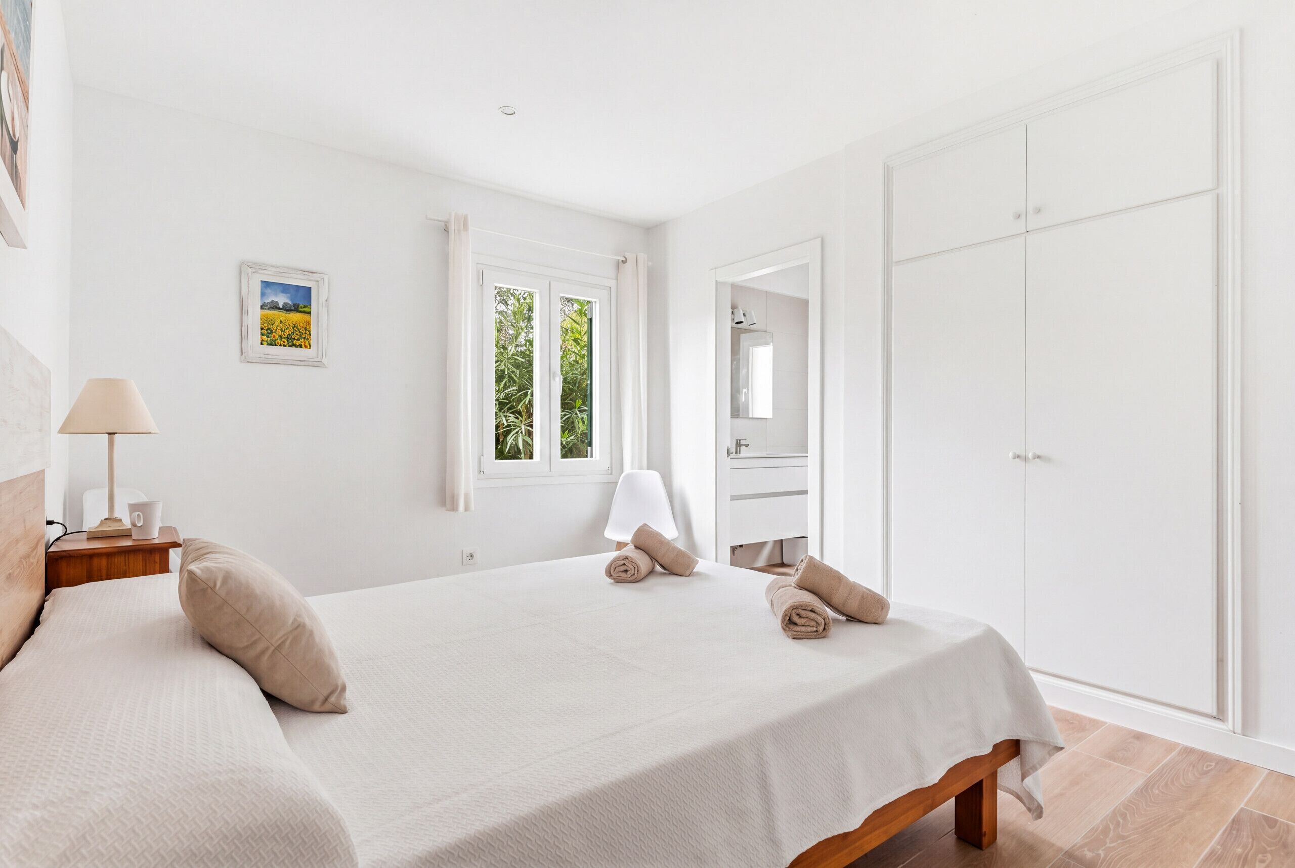 A bedroom with a bed, a nightstand, a lamp, a window, a mirror, and a wardrobe.