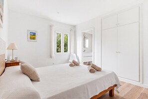 Une chambre à coucher avec un lit, une table de chevet, une lampe, une fenêtre, un miroir et une armoire.