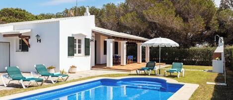 A poolside area with a swimming pool, lounge chairs, and a patio with a table and chairs.