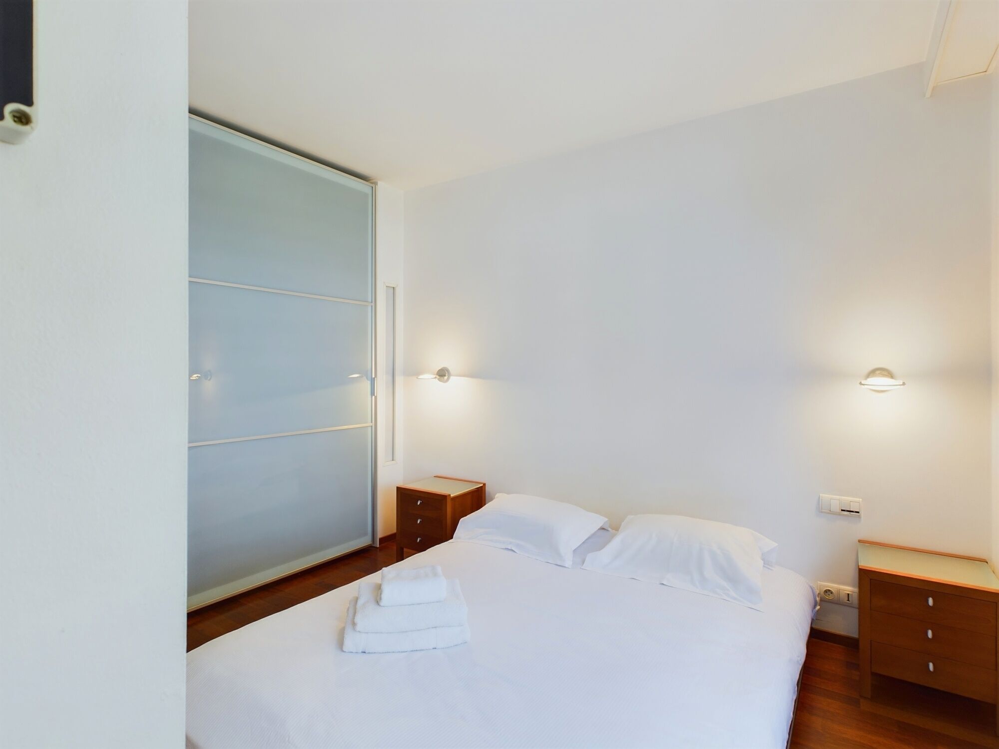 A bedroom with a bed, bedside tables, a wardrobe, and wall-mounted lights.