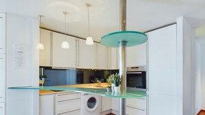 Una cocina moderna con armarios blancos, una encimera de vidrio, una lavadora y un horno de acero inoxidable.