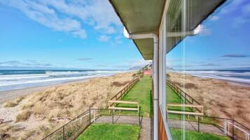 A view from a balcony overlooking a beach with a wooden walkway and a grassy area.