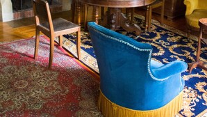 A dining room with a round wooden table, blue upholstered chairs, a chandelier, and a fireplace.