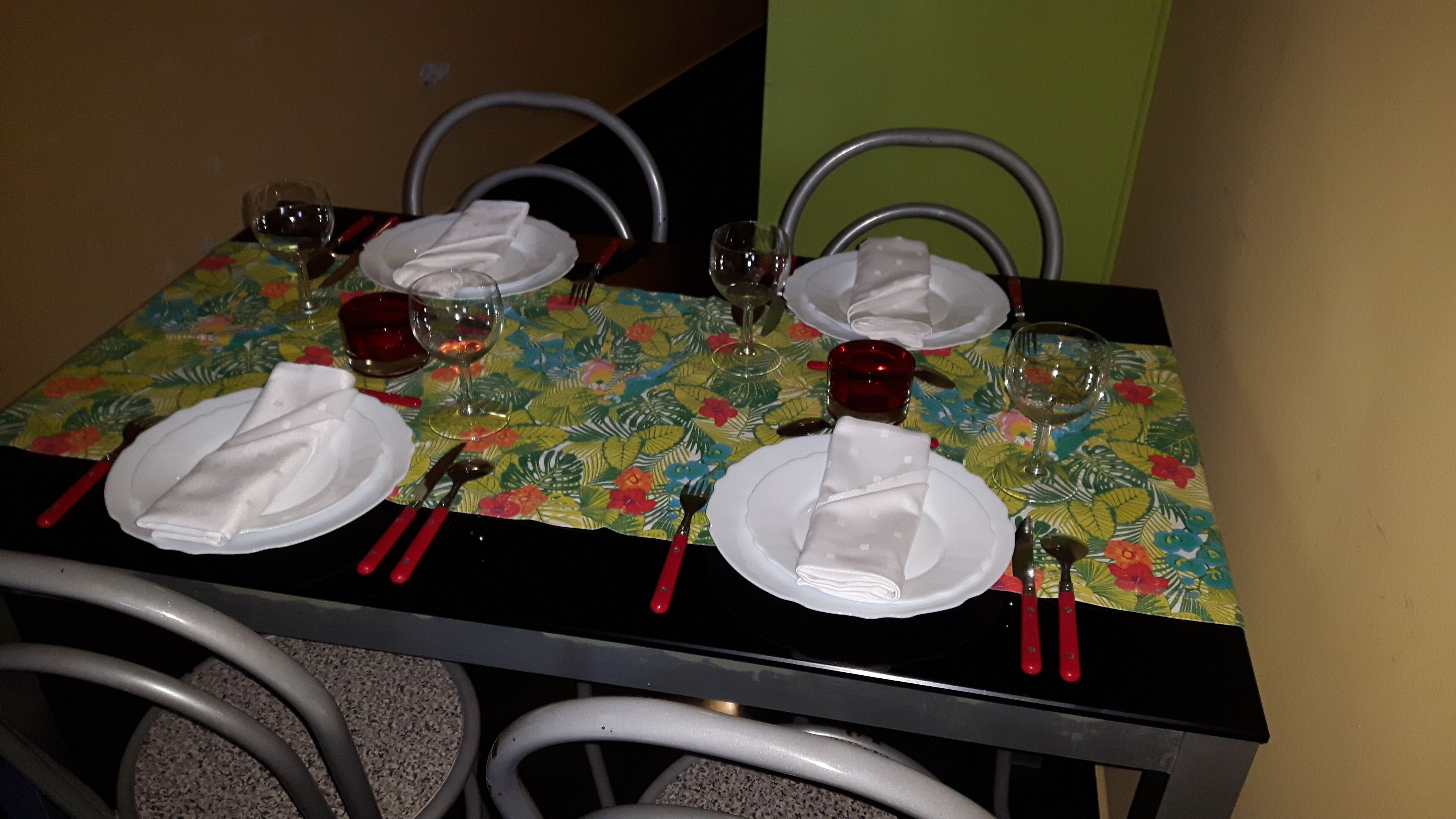 A dining table set with plates, cutlery, and wine glasses, covered by a floral tablecloth.