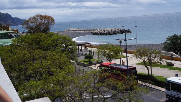 Una zona costera con un paseo pavimentado, bancos y un autobús rojo.