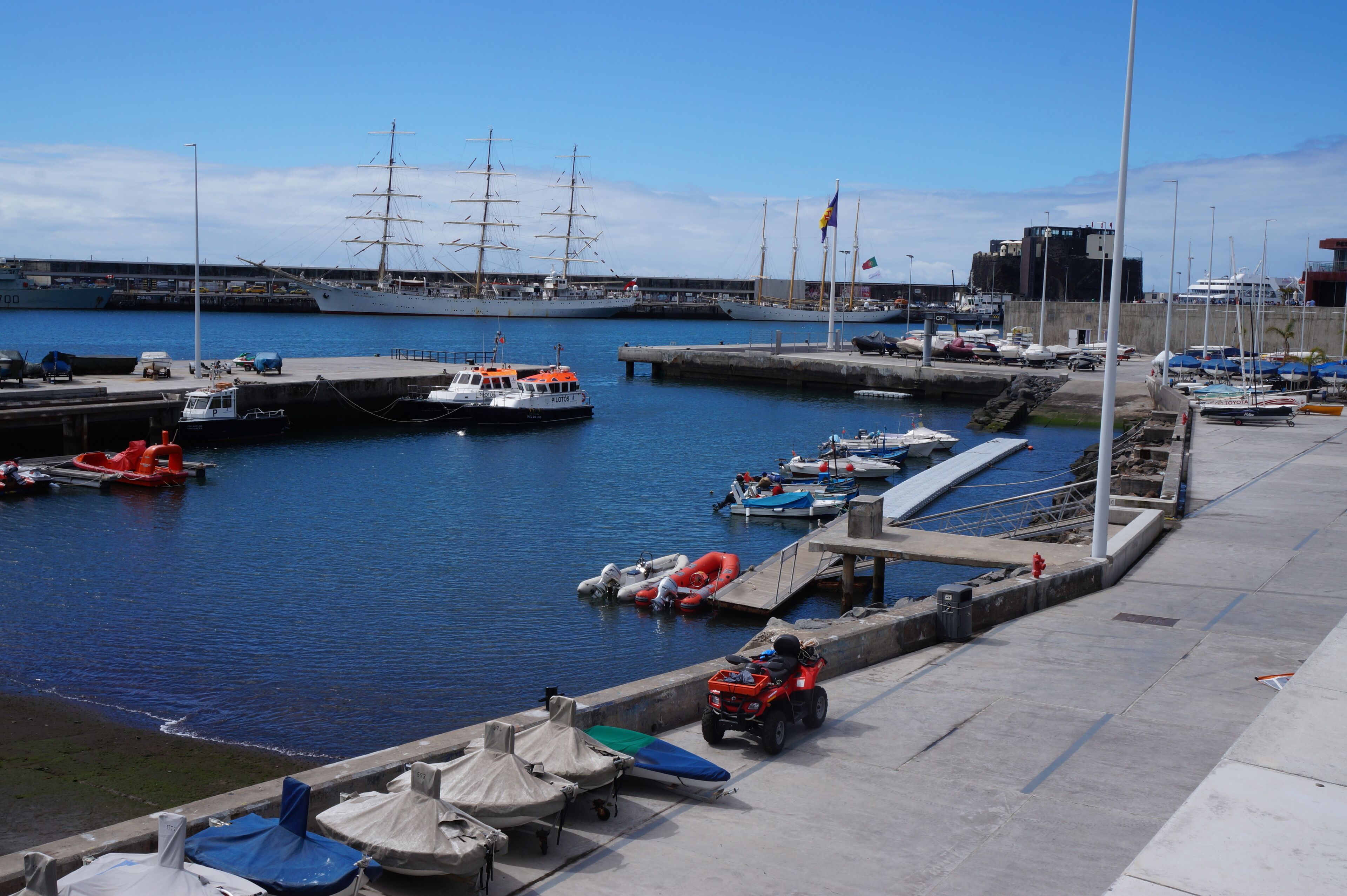 Un puerto deportivo con barcos, un buque grande y un cuatrimoto amarrado.