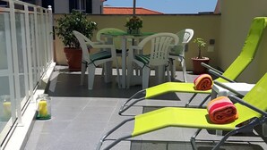 Una terraza en la azotea con sillones, una mesa y una sombrilla.