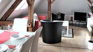Et spiseområde med et bord dækket til to personer, en sort stol og et træloft.