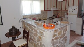 A kitchen with a central island, a dining table with chairs, a window with curtains, and a refrigerator. - Villa in a unique location with pool, beautiful gardens mountain and sea views. (Plaka)