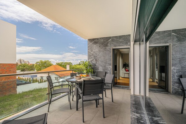 A balcony with a table and chairs, a view of the city, and a modern interior with a glass door.