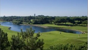 Un parcours de golf avec un étang, entouré d’arbres et sous un ciel dégagé.