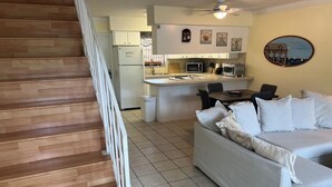 A modern living room with a wooden staircase, a white sofa, and a kitchen area with a microwave and refrigerator.