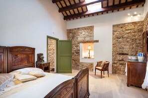 A bedroom with a wooden bed, a stone wall, a green door, a chair, and a small table with a lamp.