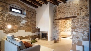 A cozy living room with a stone wall, a fireplace, and a modern sofa. - Holiday Home in Sicily for 6 People with Pool (Buseto Palizzolo)