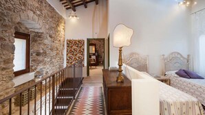 A room with a stone wall, a wooden staircase, a bed with a patterned bedspread, and a lamp. - Holiday Home in Sicily for 6 People with Pool (Buseto Palizzolo)