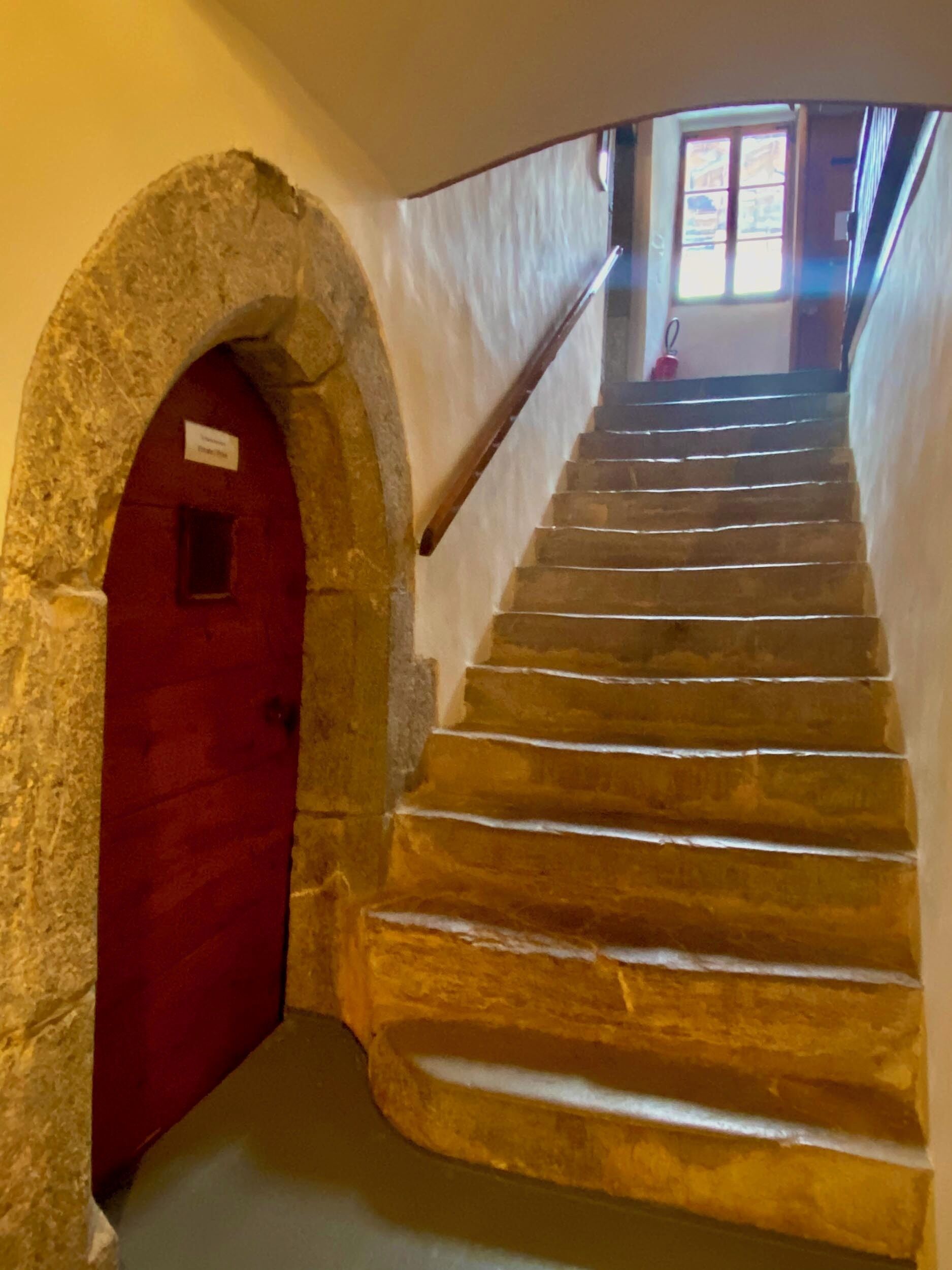 A stone staircase with a red door at the top, leading to a room with a window.