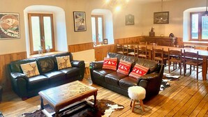 A spacious living room with a black leather sofa, a wooden dining table, and a chandelier. - Unique, charming chalet with ensuite rooms, hot tub and games room (Saint-Jean-d'Aulps)