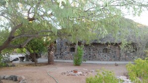 Um edifício rústico de pedra com telhado de colmo, rodeado por um jardim com pedras e plantas.