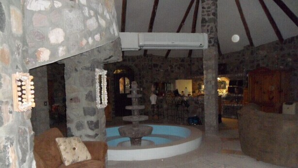 Um quarto com paredes de pedra e uma lareira de pedra, um sofá marrom, uma pequena fonte e um armário de madeira.