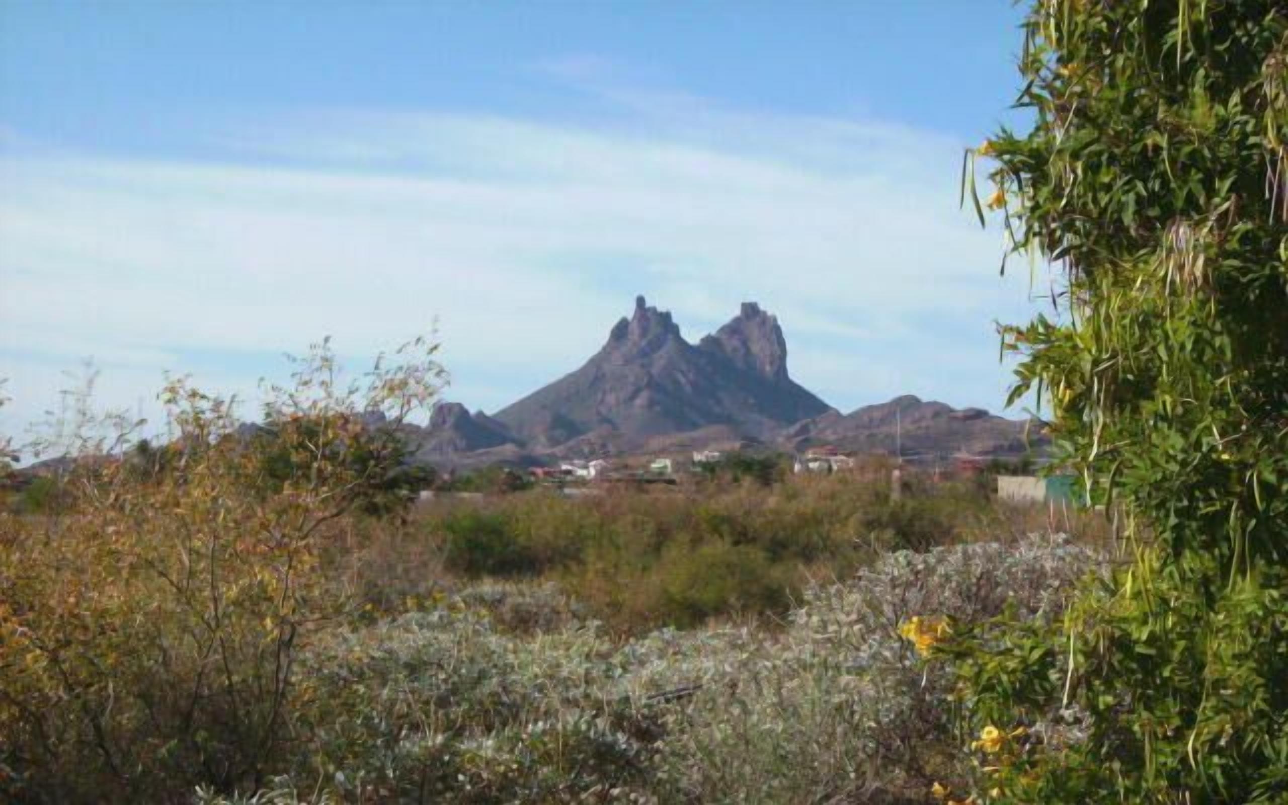 Paisaje montañoso con un pico destacado al fondo y vegetación escasa en primer plano.