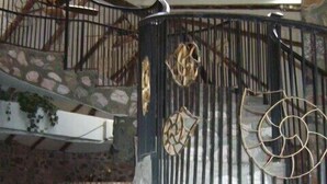 Interior de pedra com vários níveis, uma escadaria em espiral, uma fonte e detalhes em metal decorativo.