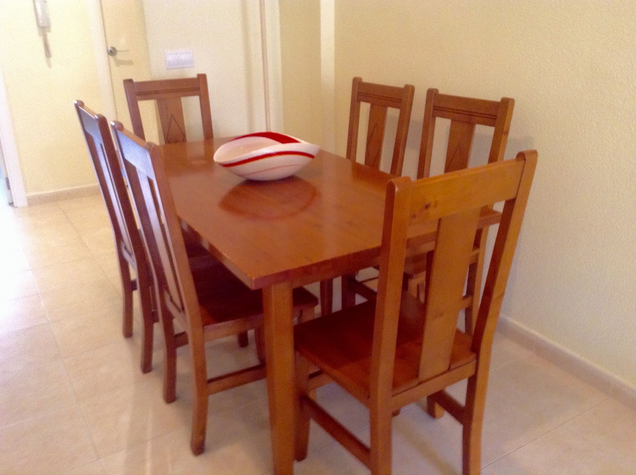 Una mesa de comedor de madera con seis sillas, un cuenco blanco con diseño rojo y un interruptor de luz en la pared.