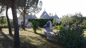 A stone building with multiple conical roofs, surrounded by trees and potted plants. - Trullo La Canonica - Itria Valley (Martina Franca)