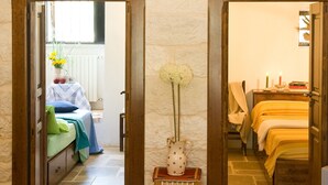 A room with a stone floor, a bed with a green blanket, a bedside table with a vase, and a wooden door leading to another room. - Trullo La Canonica - Itria Valley (Martina Franca)