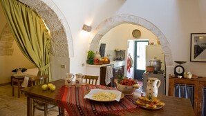 A dining area with a table set for two, a kitchen in the background, and a stone archway. - Trullo La Canonica - Itria Valley (Martina Franca)
