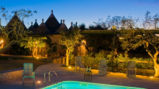 A swimming pool with lounge chairs and a stone building with multiple pointed roofs in the background. - Trullo La Canonica - Itria Valley (Martina Franca)
