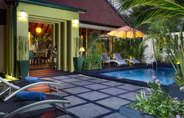 Un área junto a la piscina con sillones de descanso, una piscina pequeña y plantas en macetas.