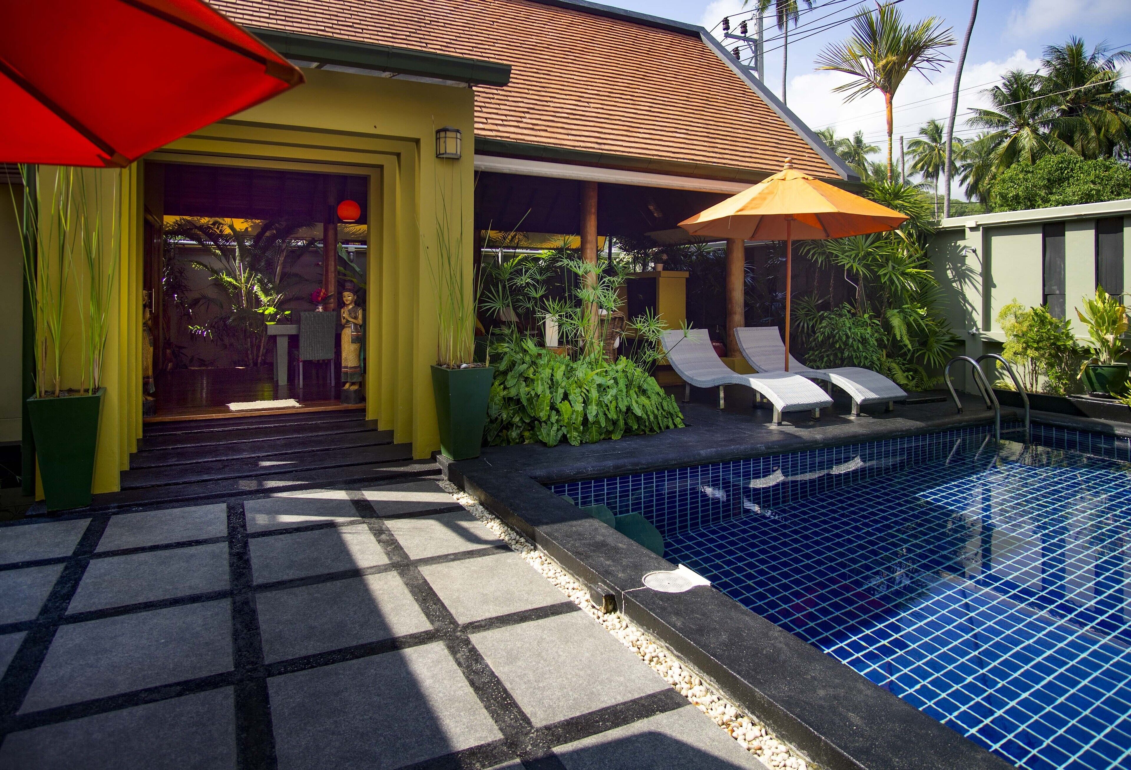 Zona junto a la piscina con un estanque de baldosas, sillones de descanso y sombrillas.