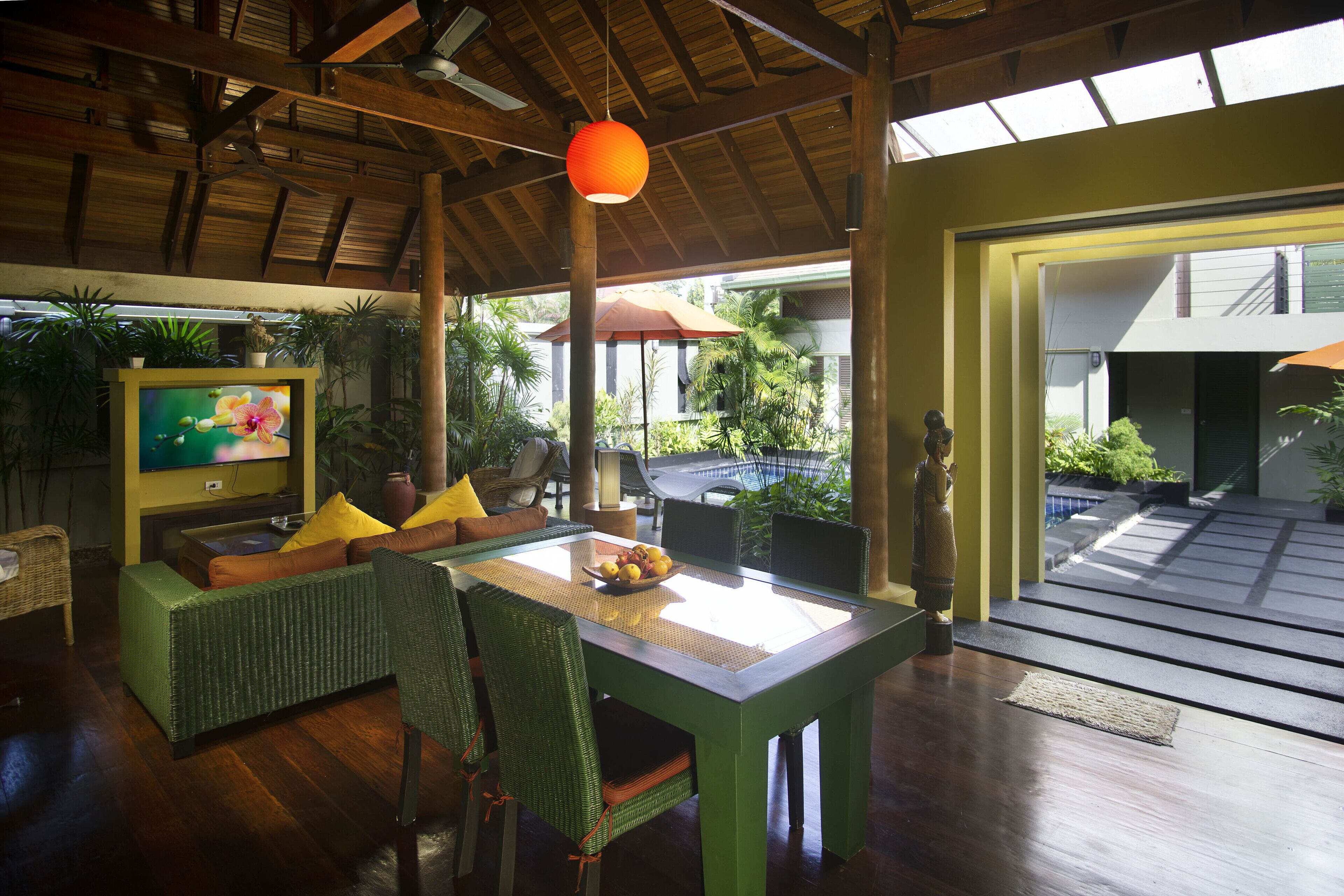 A spacious room with a wooden ceiling, a dining table with chairs, a television, and various plants.