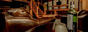 A cozy lounge area with leather seating, a wooden staircase, and a bar area with bottles and glasses.