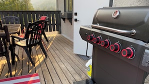 A barbecue grill with multiple controls, a wooden deck, outdoor furniture, and a view of trees in the background. - One Of A Kind Vacation Rental Located By The Base Of Boulder Mountain! (Columbia-Shuswap B)