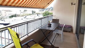 A balcony with a striped awning, a table with a potted plant, and a chair. - GOLFE JUAN, 150 m from the beach, F2, bright, 43m2, balcony 14m2, sea view + garage (Vallauris)