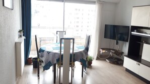A dining area with a table and chairs, a TV, and a cabinet. - GOLFE JUAN, 150 m from the beach, F2, bright, 43m2, balcony 14m2, sea view + garage (Vallauris)