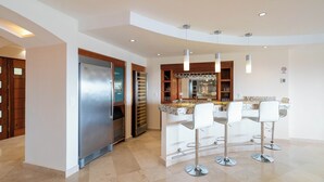 Una cocina moderna con refrigerador empotrado, encimera de mármol y barra con taburetes blancos.