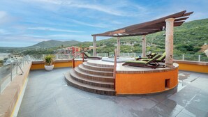 Una terraza en la azotea con pérgola, mobiliario exterior y vistas del paisaje circundante.
