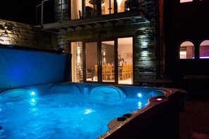 A hot tub with a stone exterior and a view of a dining area through glass doors.