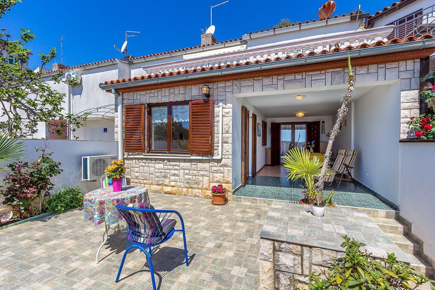 A house with a tiled patio, a small table with a colorful tablecloth, and a blue chair.
