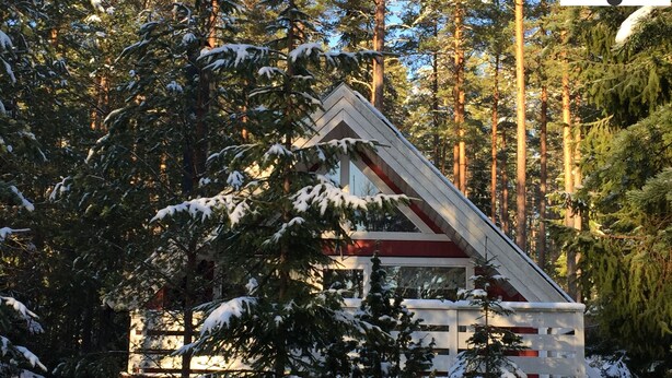 Une cabane aux murs rouges et blancs, entourée d’arbres couverts de neige et d’une zone boisée.
